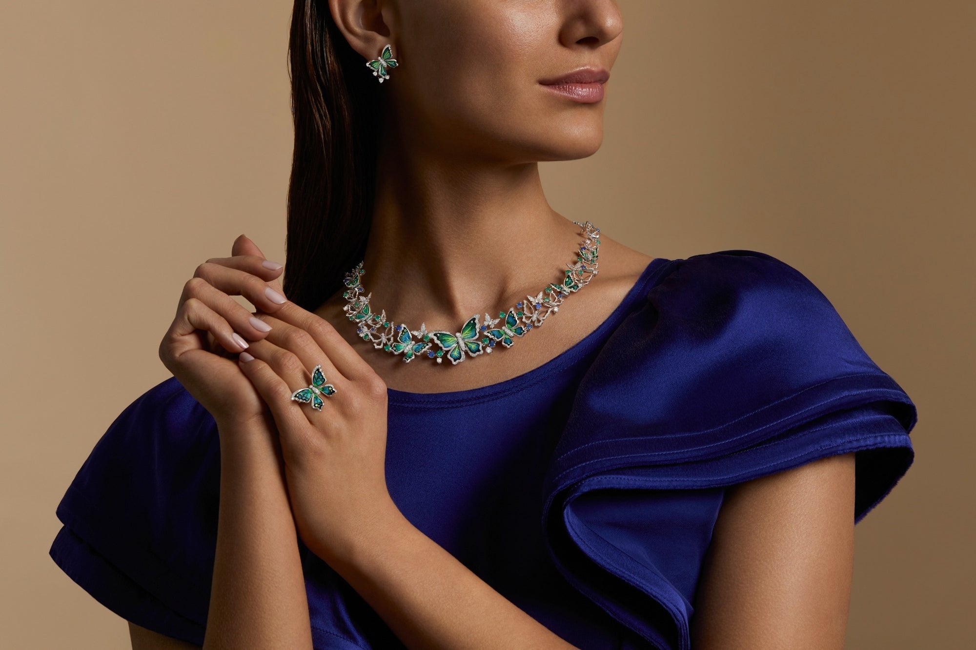 Woman wearing a blue dress with green jewelry on a beige background